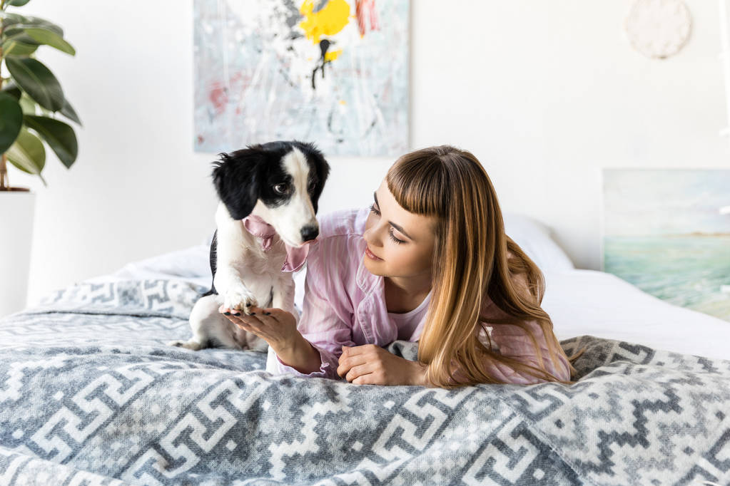 retrato de la mujer sosteniendo cachorros pata mientras yacía en la cama juntos en la mañana
 - Foto, imagen