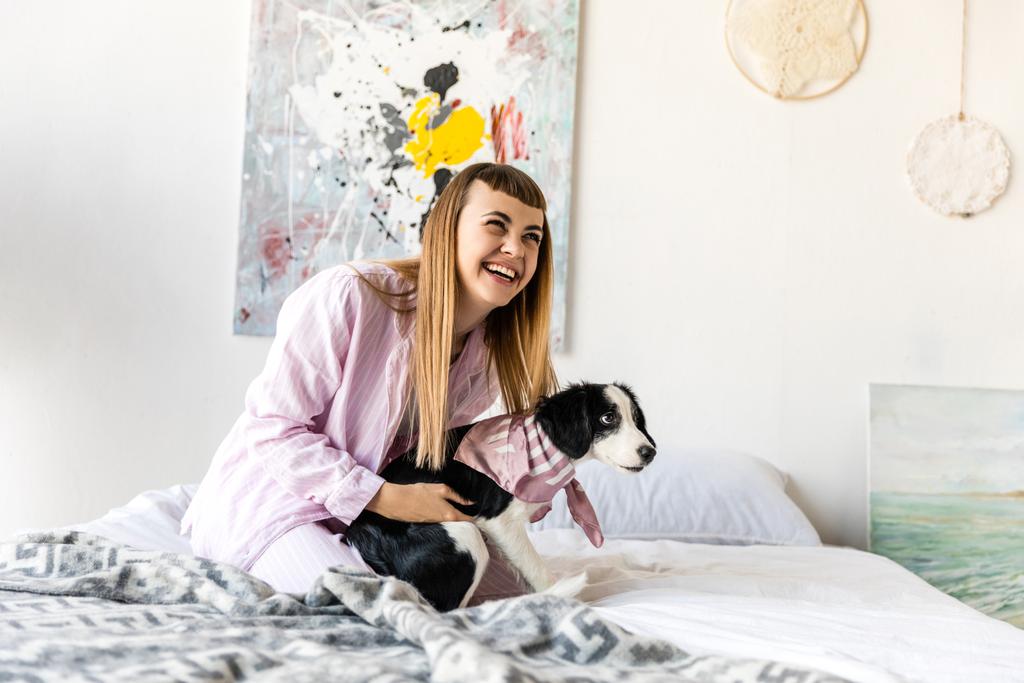 mulher feliz em pijama e filhote de cachorro bonito descansando na cama de manhã em casa
 - Foto, Imagem