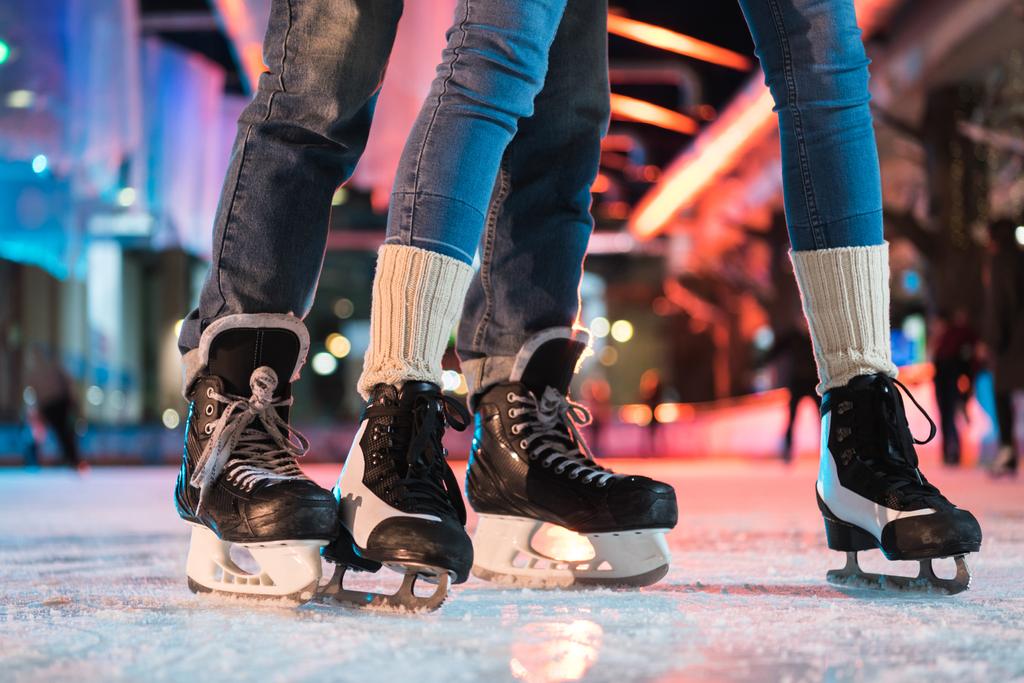 close-up partial view of young couple in skates ice skating on rink - Photo, Image