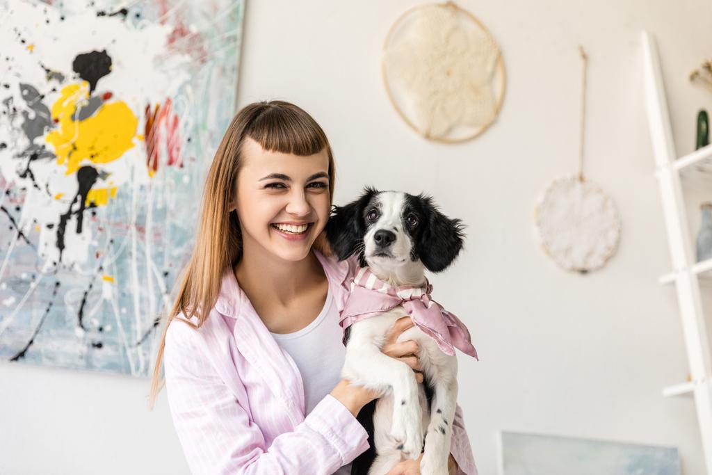 portrait of happy woman holding adorable puppy in hands at home - Photo, Image