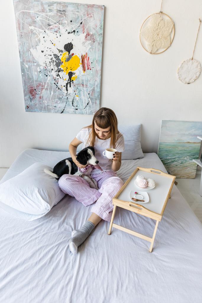 donna che beve caffè mentre riposa a letto insieme al cucciolo
 - Foto, immagini