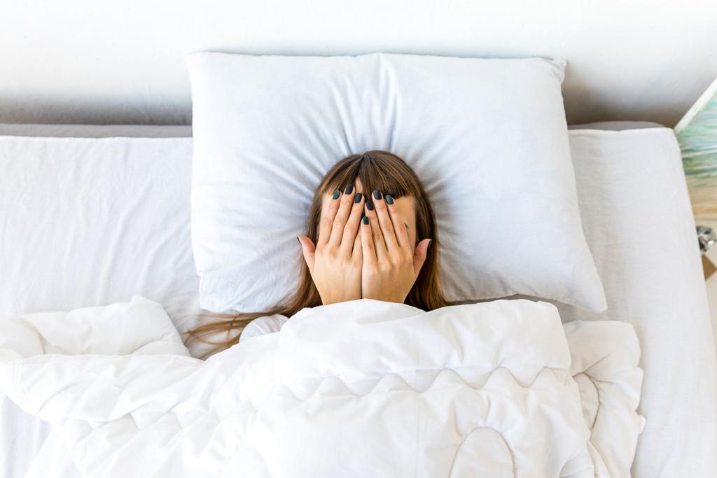 скрытый вид женщины, покрывающей лицо руками, лежащей в постели
 - Фото, изображение