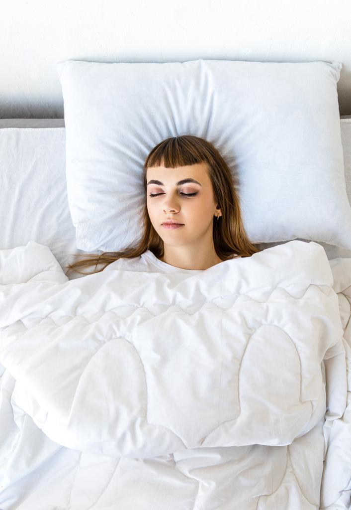 κάτοψη της νεαρής γυναίκας που κοιμάται στο κρεβάτι πρωί - Φωτογραφία, εικόνα