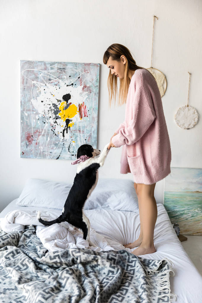 boční pohled na mladou ženu a štěně tančí na posteli spolu ráno - Fotografie, Obrázek