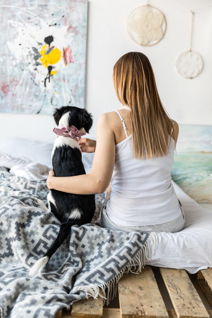 Achteraanzicht van de vrouw en kleine pup zittend op bed samen thuis - Foto, afbeelding