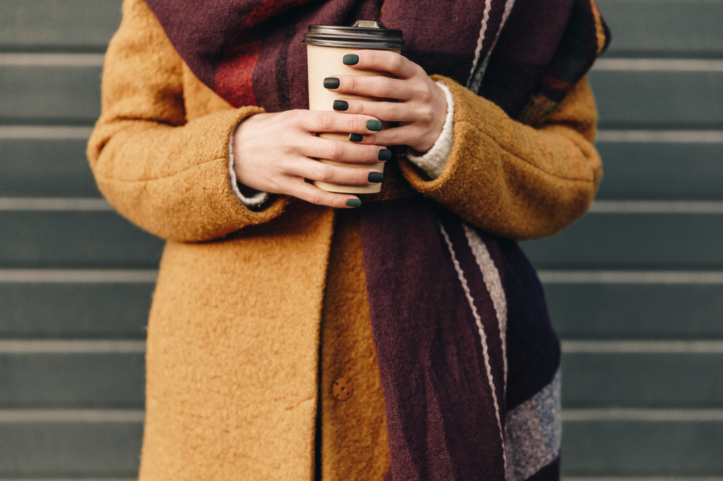 手にコーヒーを持って秋のジャケットの女性のショットをトリミング - 写真・画像