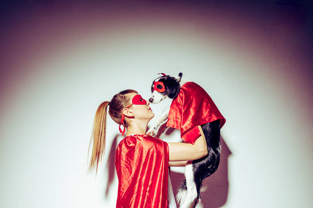 vista laterale di giovane donna e cucciolo in maschere rosse e mantelle
 - Foto, immagini