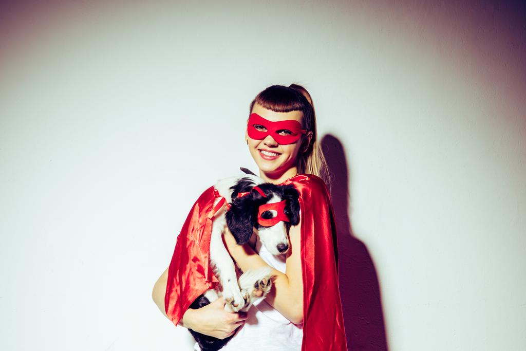 Portret van lachende vrouw bedrijf puppy in superheld kostuum - Foto, afbeelding