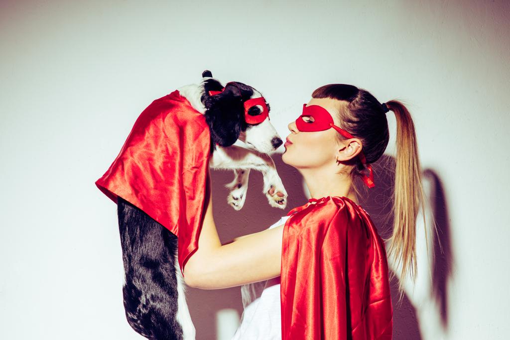Widok z boku kobieta całuje szczeniak w strój superbohatera - Zdjęcie, obraz