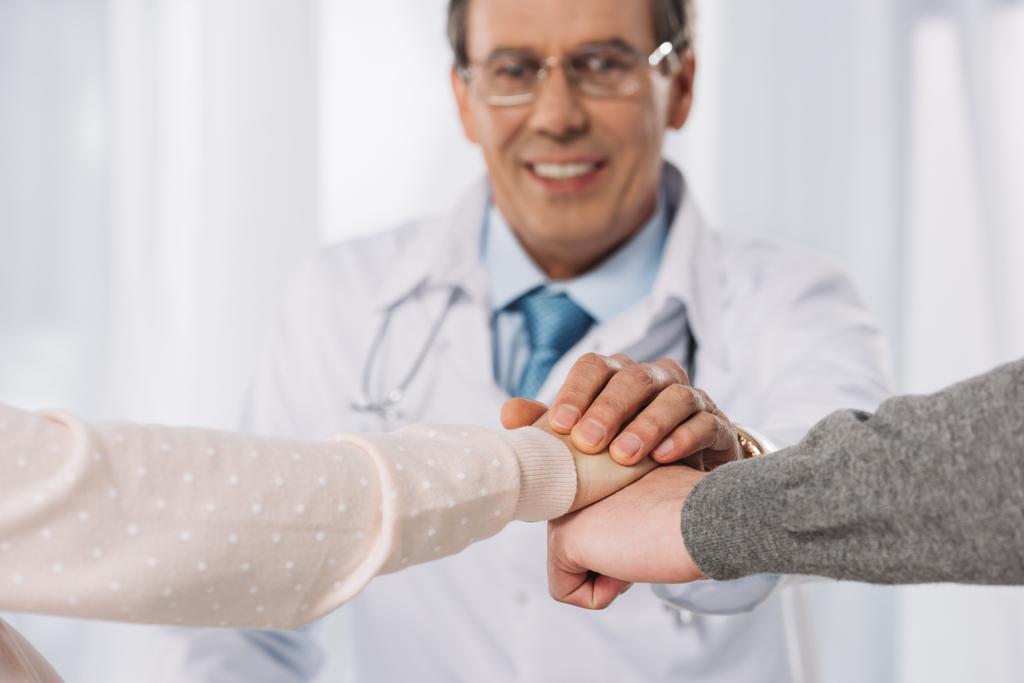 abgeschnittenes Bild von Arzt und zwei Patienten, die sich an den Händen halten - Foto, Bild