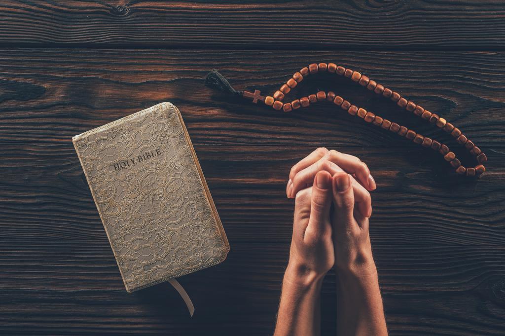 abgeschnittenes Bild einer Frau, die mit Rosenkranz und heiliger Bibel am Tisch sitzt und betet   - Foto, Bild
