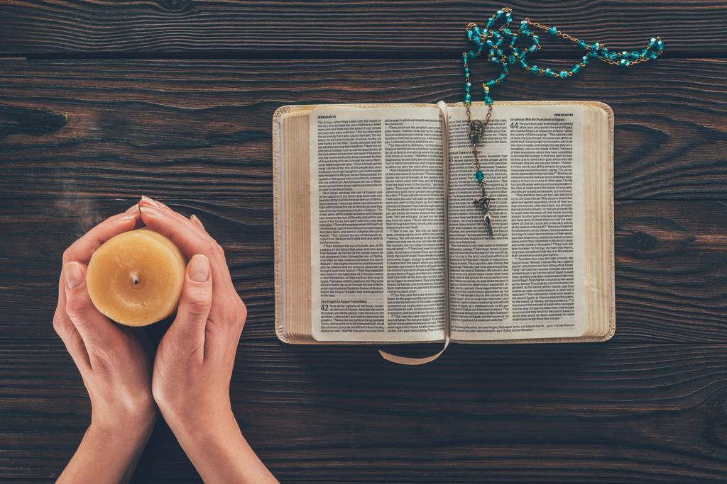 περικομμένη εικόνα γυναίκας κρατώντας κερί παραπάνω ξύλινο τραπέζι με την Αγία Γραφή - Φωτογραφία, εικόνα