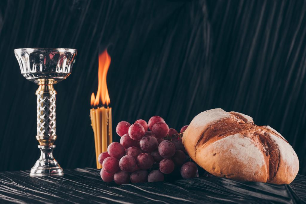 Brot mit Trauben, Kelch und Kerzen auf schwarzem Stoff, heilige Kommunion  - Foto, Bild