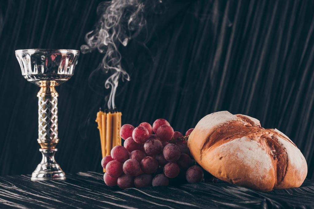 Brot, Trauben, Kerzen und Kelch auf dunklem Stoff für das Abendmahl  - Foto, Bild