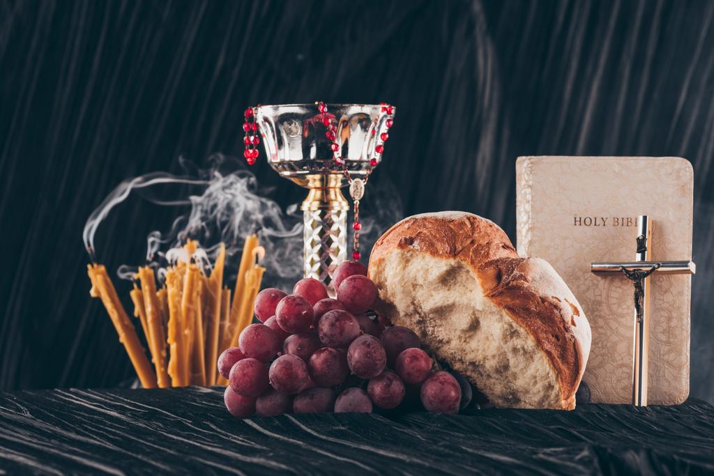 Raamattu ja kristillinen risti kynttilöillä ja maljalla tummalla raidallisella pöydällä pyhää ehtoollista varten
 - Valokuva, kuva