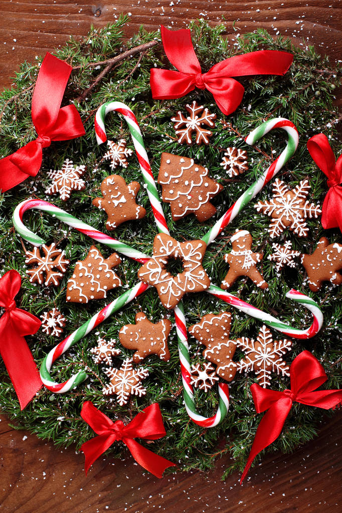 Χριστουγεννιάτικο στεφάνι με έλατο με μπισκότα πιπεροριζών, μπαστούνια καραμέλας και κόκκινη κορδέλα τόξα. Με το ξύλινο υπόβαθρο. Snowy.Closeup - Φωτογραφία, εικόνα