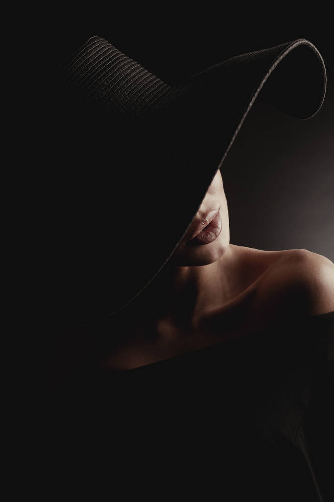 Dramatisches Studioporträt einer eleganten Frau mit schwarzem Hut und schwarzem Kleid. verstecktes halbes Gesicht. - Foto, Bild
