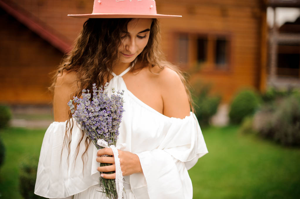 schöne lockige Frau in weißem Kleid mit Lavendelstrauß gekleidet - Foto, Bild