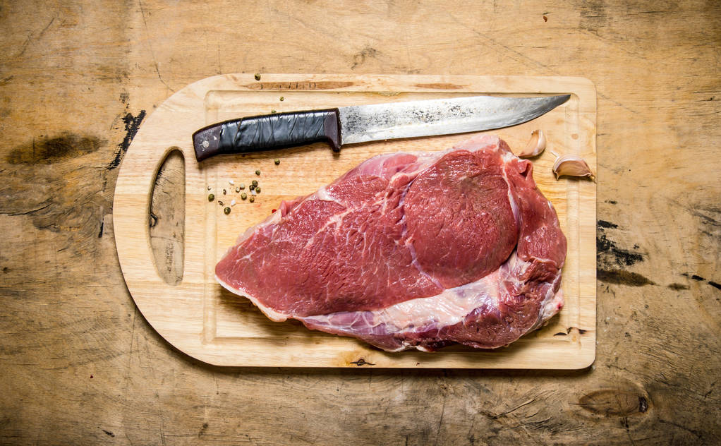 Un trozo de carne cruda con cuchillo sobre tabla de madera
. - Foto, Imagen