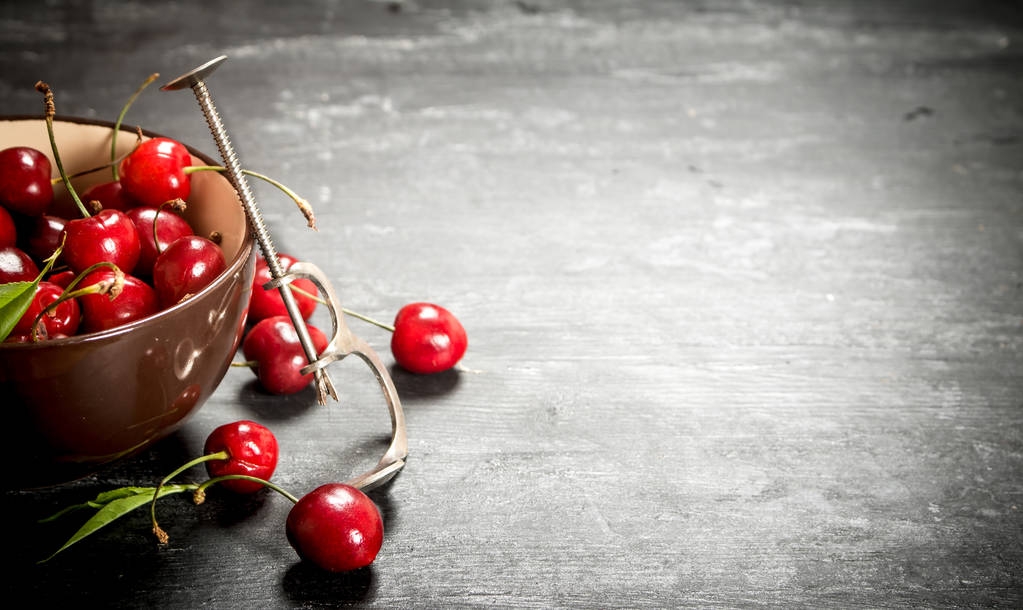 Cherry v poháru a kovovým nástrojem pro třešně a višně. - Fotografie, Obrázek