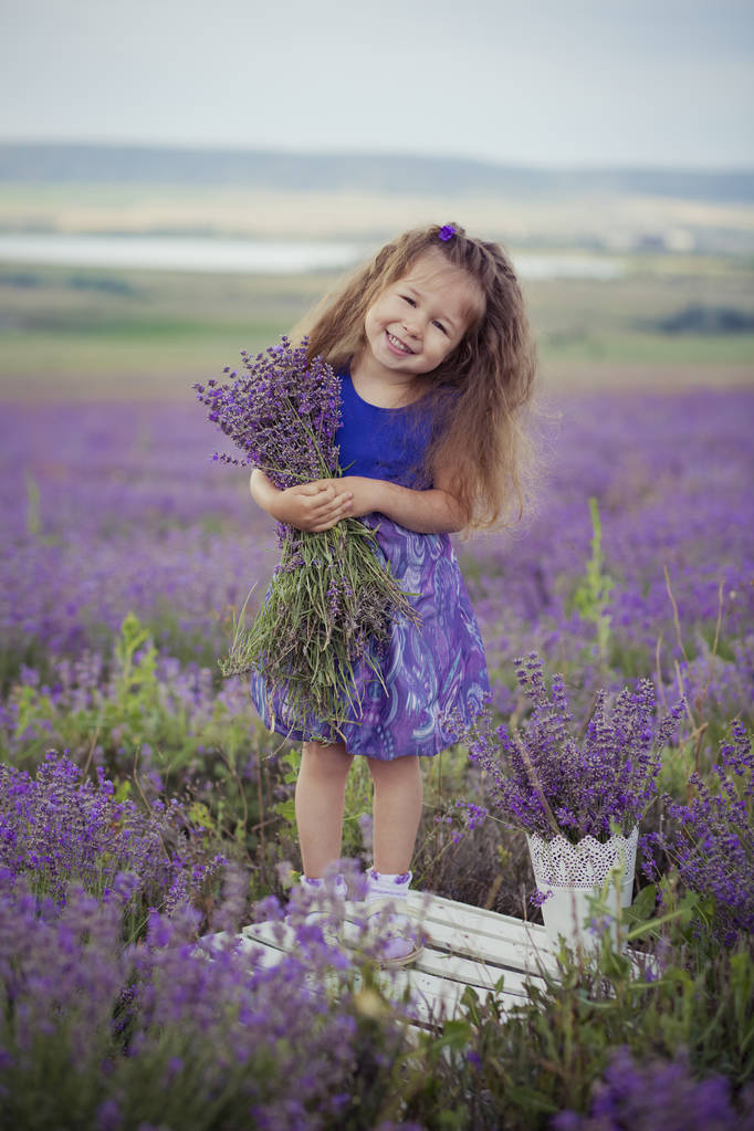 Dość młoda dziewczyna siedzi w lawendowym polu w ładne kapelusz Kanotier fioletowy kwiat na nim. - Zdjęcie, obraz