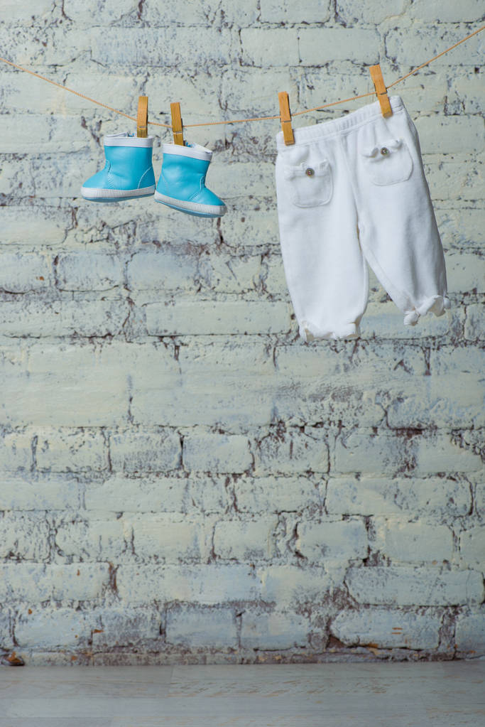 Дитячі черевики і колготки сухі на мотузці на білій цегляній стіні
. - Фото, зображення