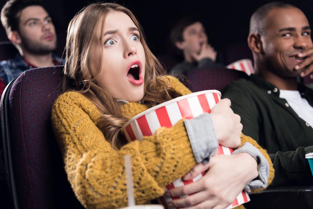 geschokt meisje houden grote mand van popcorn en kijken naar film in de bioscoop - Foto, afbeelding