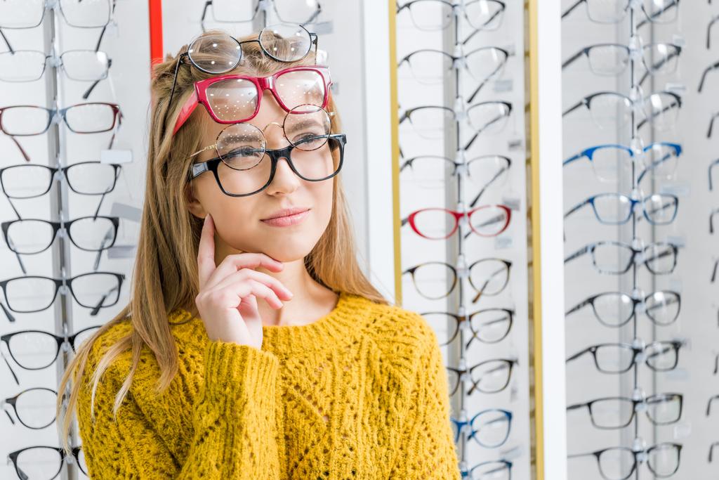 joven chica pensativa la elección de las gafas en óptica
 - Foto, Imagen