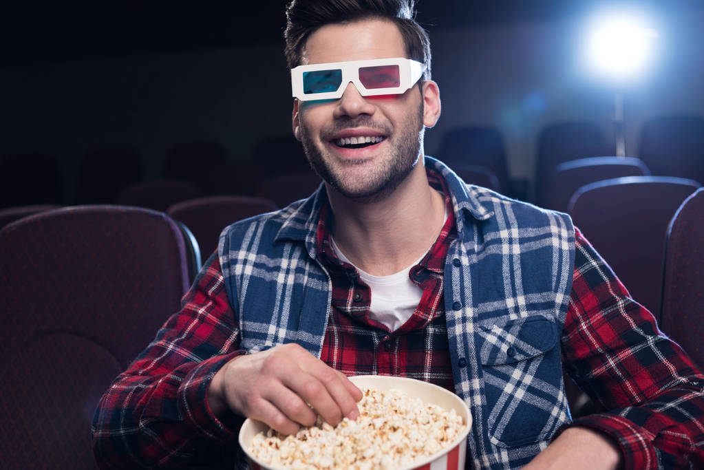 улыбающийся мужчина в 3D очках с попкорном, смотрящим кино в кино
 - Фото, изображение