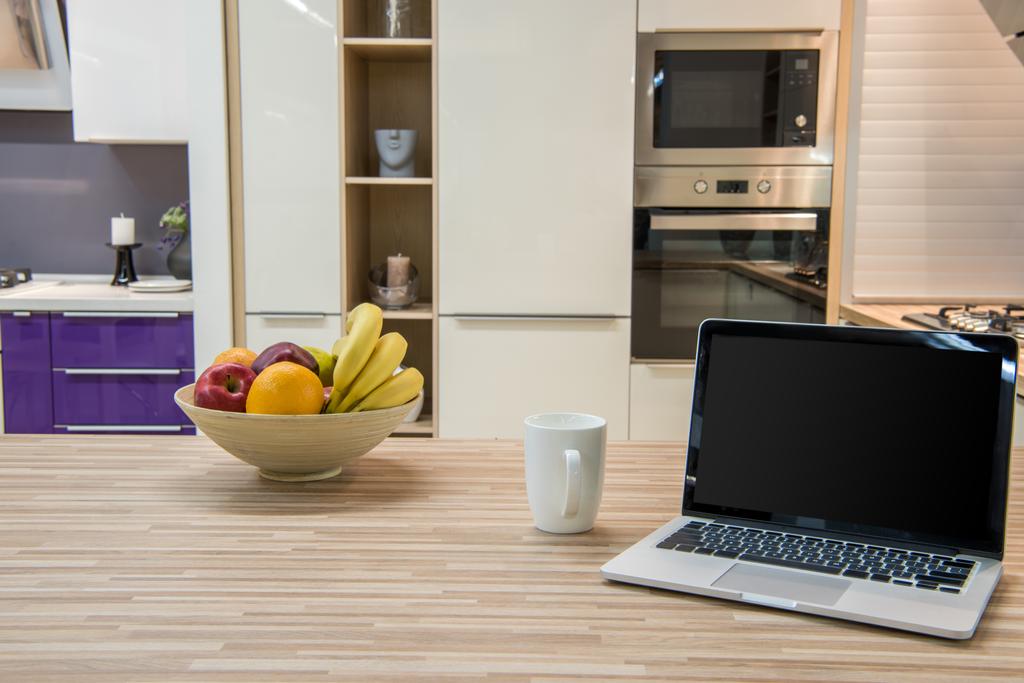 Gemütliche moderne Kücheneinrichtung mit Laptop und Früchten in Schüssel - Foto, Bild