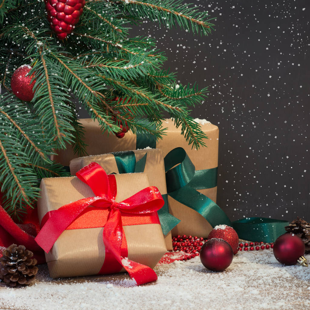 Weihnachtsurlaub Hintergrund. Geschenke, Weihnachtsmannmütze und Dekoration unter einem Weihnachtsbaum auf einem Holzbrett. Kopierraum auf Kreidetafel. - Foto, Bild