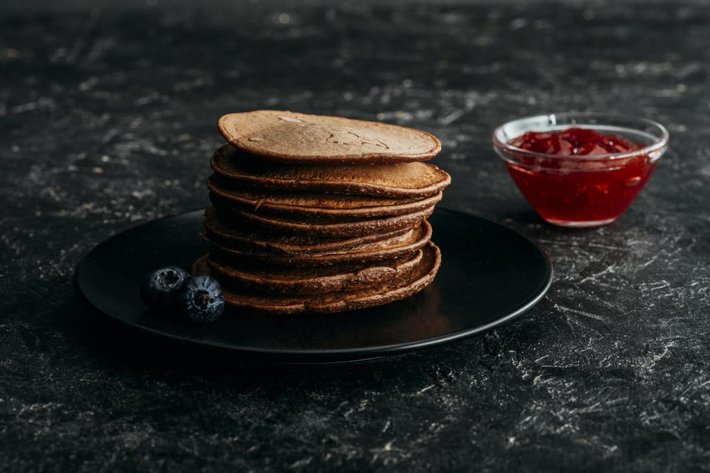 gestapelte Schokoladen-Pfannkuchen mit Blaubeeren und Marmelade - Foto, Bild