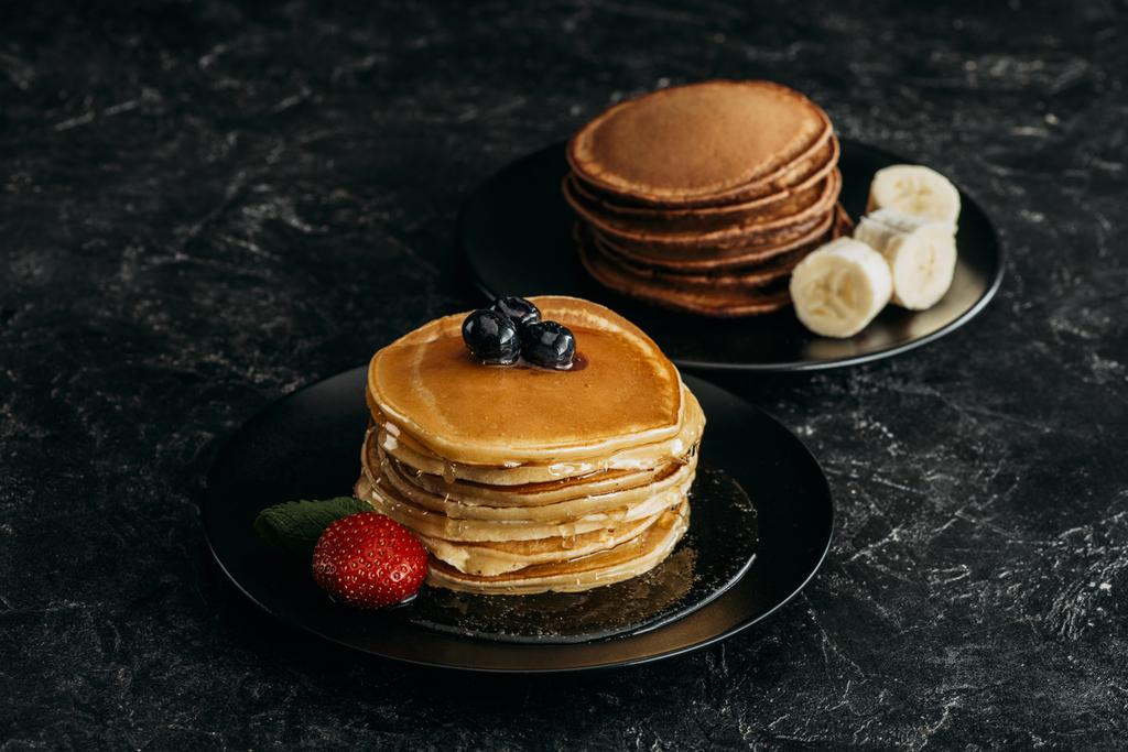 plates with stacks of tasty pancakes with fruits on black table - Photo, Image