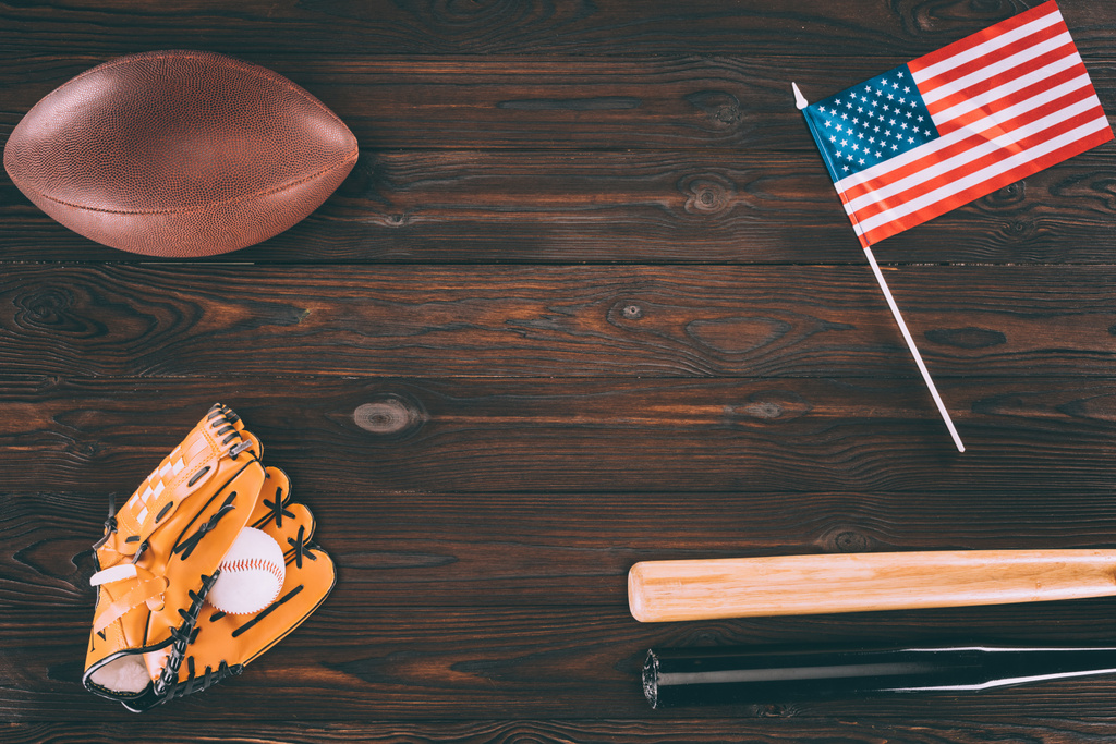 верхний вид на нас флаг, мяч для регби, бейсбольные биты и перчатки с мячом на деревянном столе
 - Фото, изображение