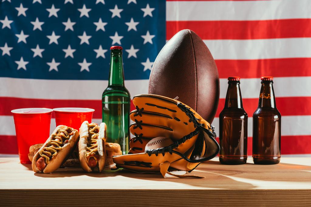 lähikuva oluesta hot dogien ja urheiluvälineiden kanssa lippumme takana
   - Valokuva, kuva