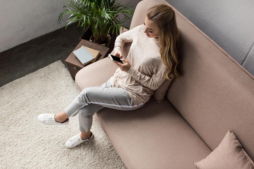 μεγάλη γωνία προβολής νεαρής γυναίκας χρησιμοποιώντας smartphone, ενώ κάθεται στον καναπέ στο σπίτι - Φωτογραφία, εικόνα