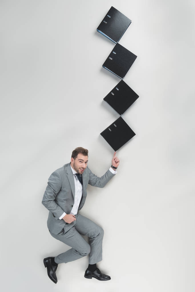 vista aérea del hombre de negocios sosteniendo pila de carpetas en un dedo aislado en gris
 - Foto, imagen