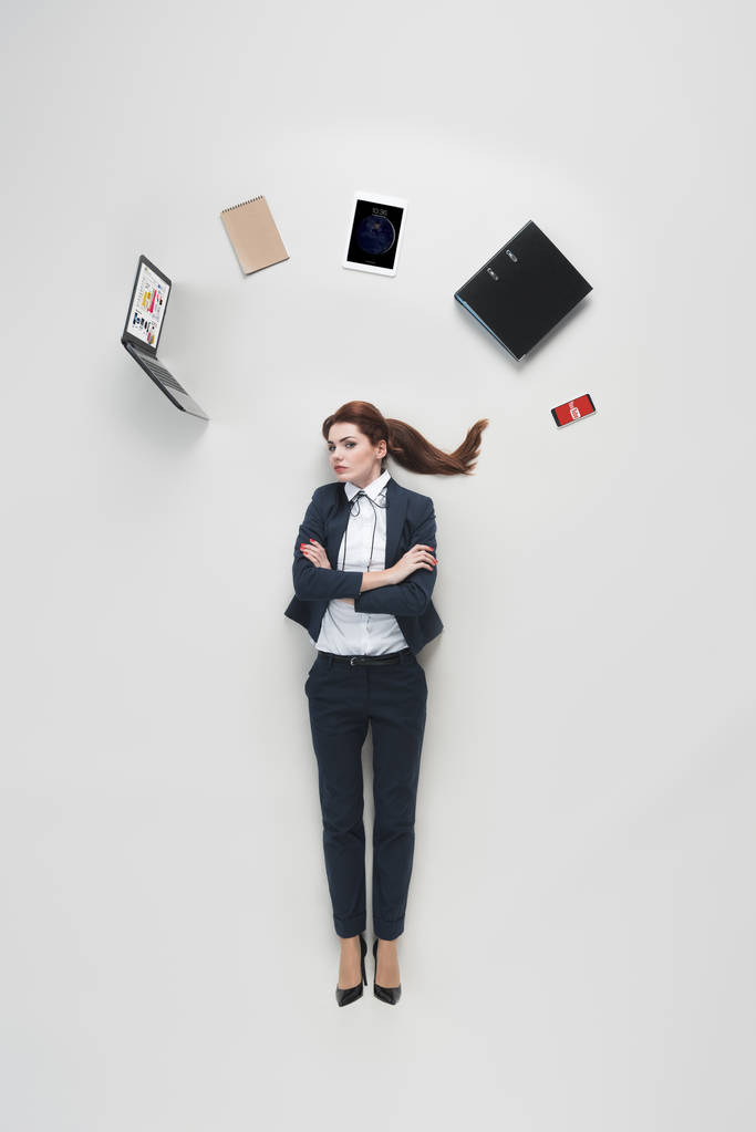 vista aérea de la mujer de negocios con varios suministros de oficina por encima de la cabeza aislado en gris
 - Foto, Imagen