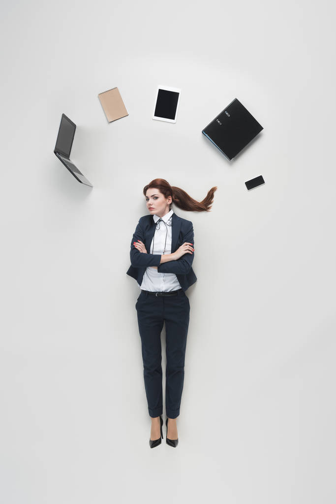 над головой бизнесвумен с различными офисными принадлежностями, изолированными на сером
 - Фото, изображение