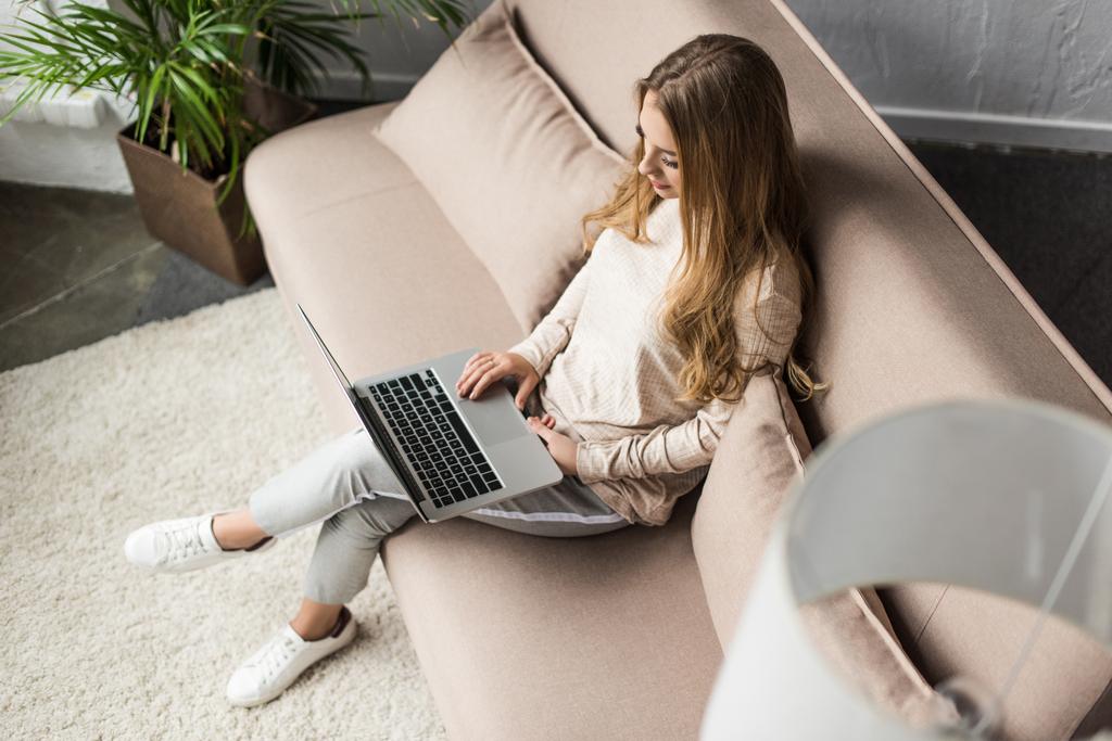 vista de ángulo alto de la mujer joven que trabaja con el ordenador portátil en el sofá
 - Foto, imagen