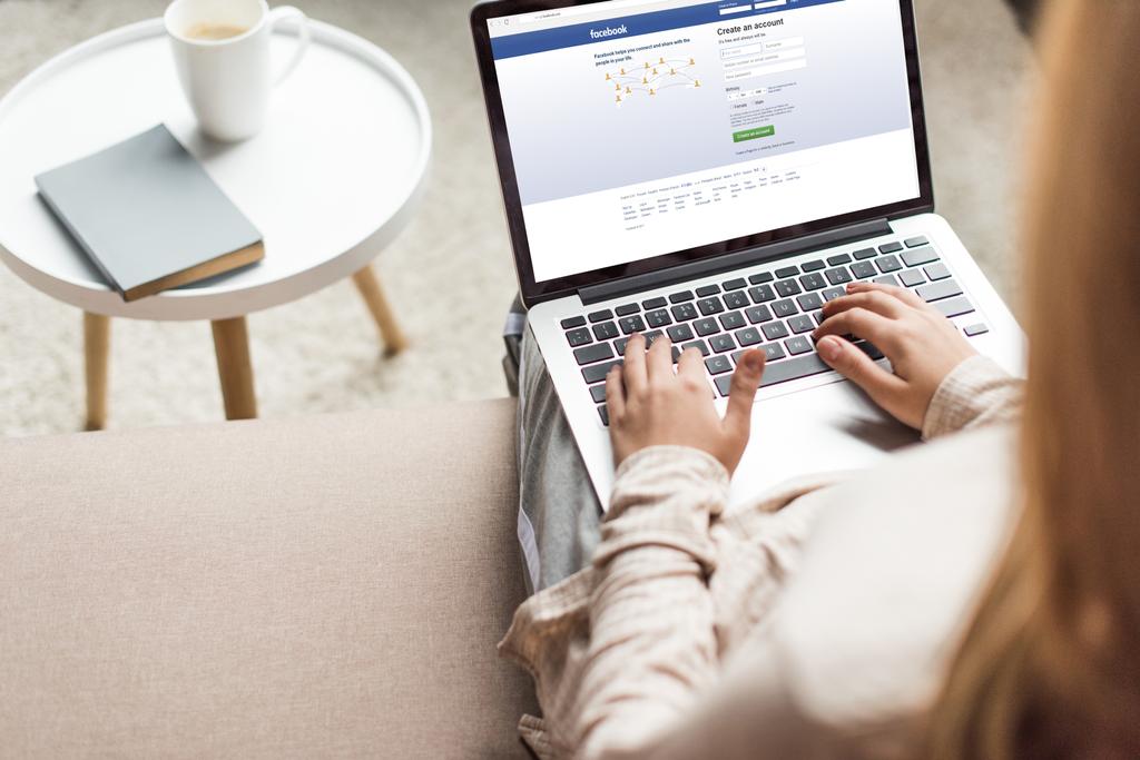 cropped shot of woman at home sitting on couch and using laptop with facebook on screen - Photo, Image