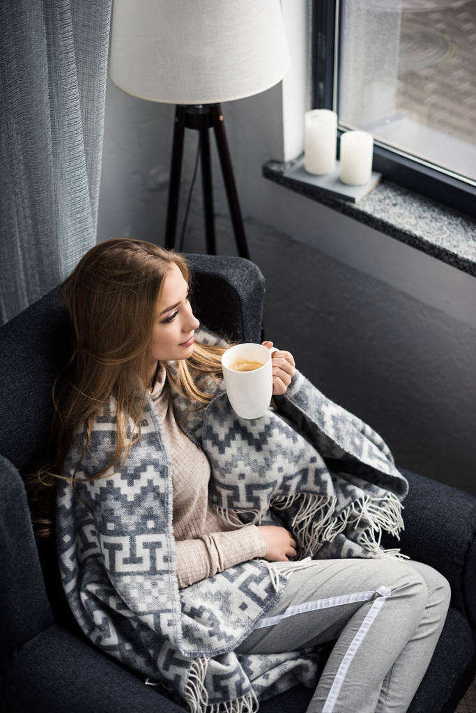 высокий угол зрения красивой молодой женщины, пьющей кофе в уютном кресле с одеялом
 - Фото, изображение