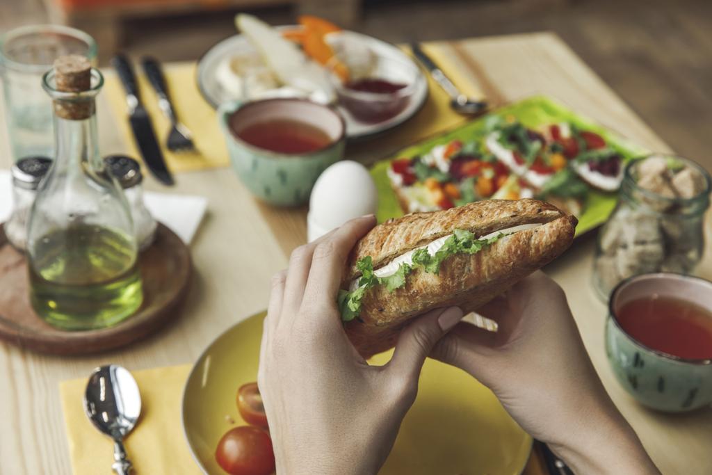 primer plano vista parcial de la persona comiendo sándwich fresco sabroso en el desayuno
  - Foto, imagen