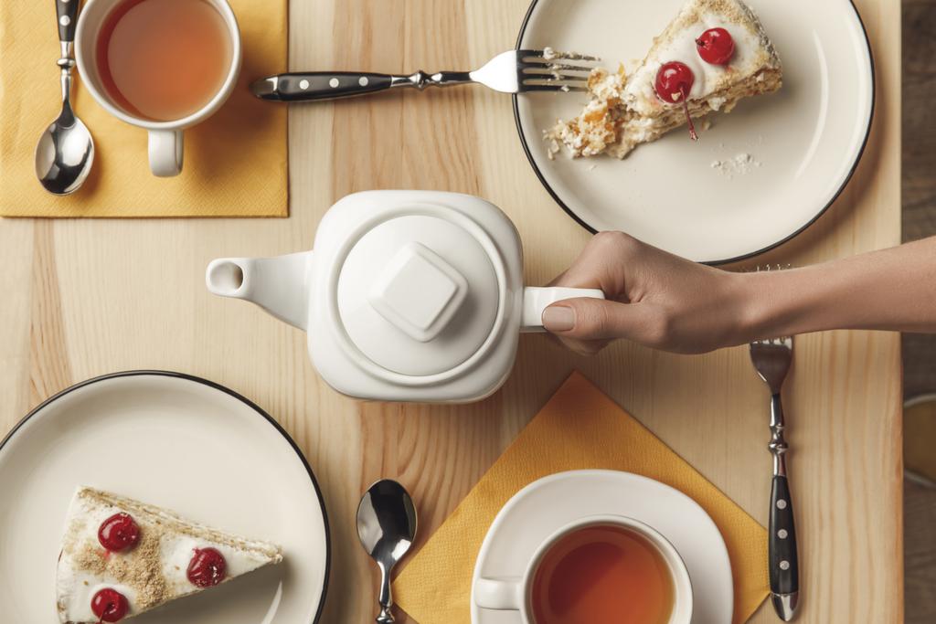 bovenaanzicht van houder theepot en thee set met gebak op tafel - Foto, afbeelding