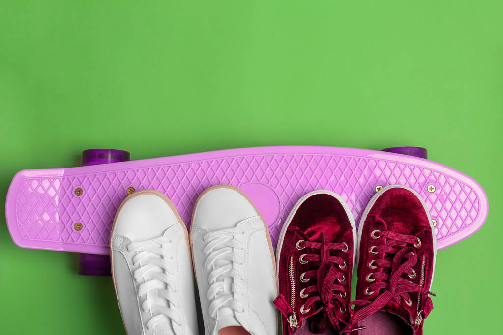 Female sport shoes with skateboard on color background - Photo, Image