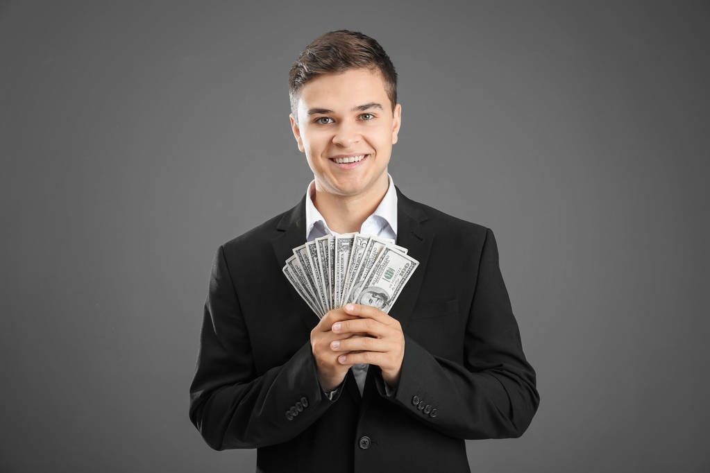 Fiatal üzletember, a dollár számlák a szürke háttér - Fotó, kép