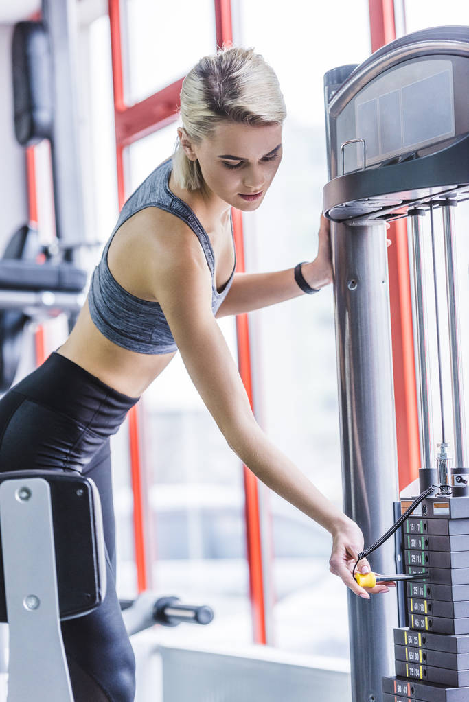 спортивна молода жінка додає ваги на тренажерному автоматі
 - Фото, зображення