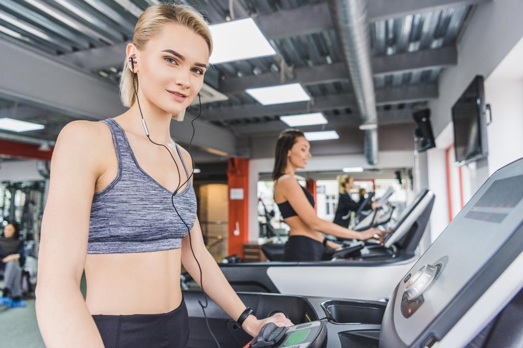 attraktive sportliche Frau läuft mit Kopfhörern auf dem Laufband im Fitnessstudio - Foto, Bild