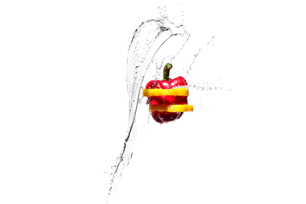 κόκκινη και κίτρινη πιπεριά φέτες σε πιτσιλιές νερού που απομονώνονται σε λευκό - Φωτογραφία, εικόνα