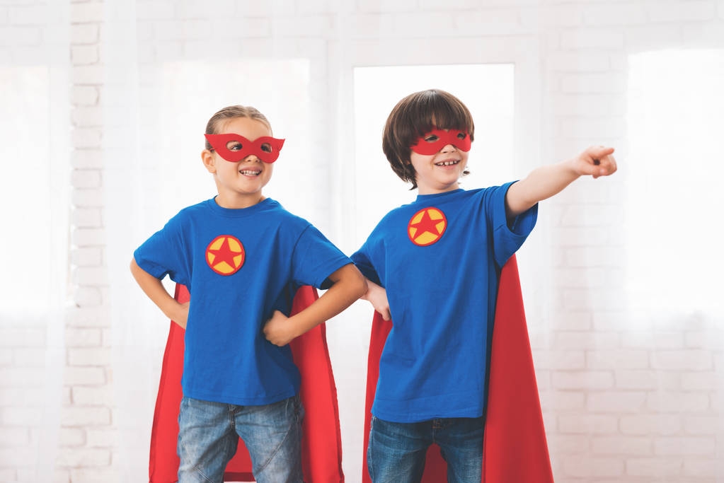 スーパー ヒーローの赤と青のスーツの子どもたち。彼らのマスク。子供たちの明るい部屋でポーズ. - 写真・画像